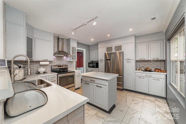 kitchen featuring wall chimney range hood, appliances with stainless steel finishes, light countertops, gray cabinets, and a kitchen island