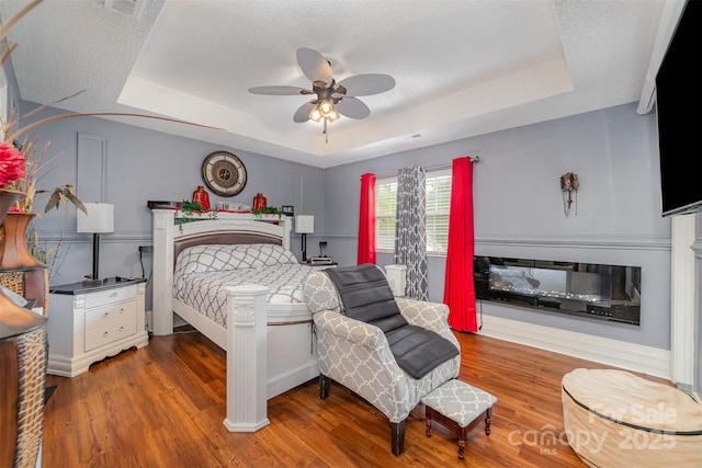 bedroom with baseboards, wood finished floors, and a tray ceiling