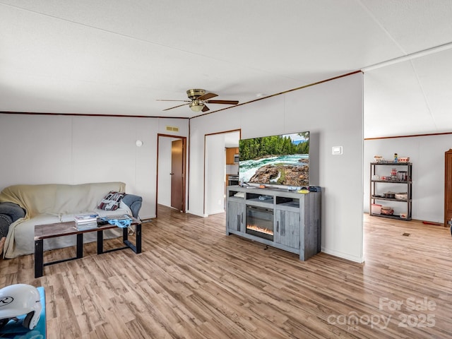 living area with a glass covered fireplace, ceiling fan, and wood finished floors