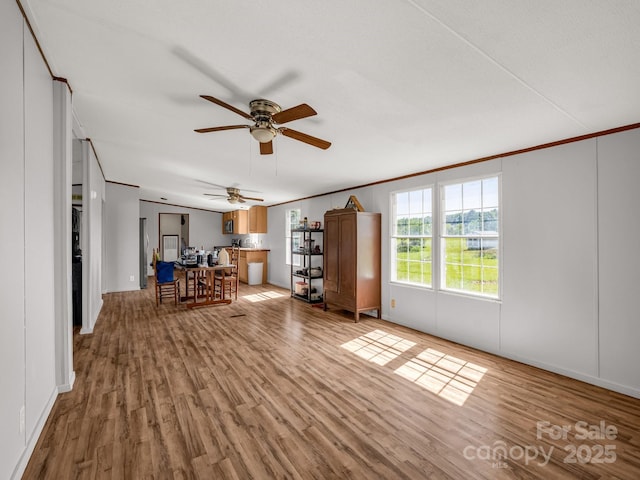 living area with light wood-style floors, ornamental molding, baseboards, and a ceiling fan