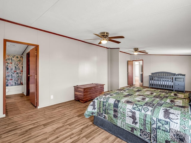 bedroom with crown molding, a ceiling fan, a decorative wall, and light wood-style floors