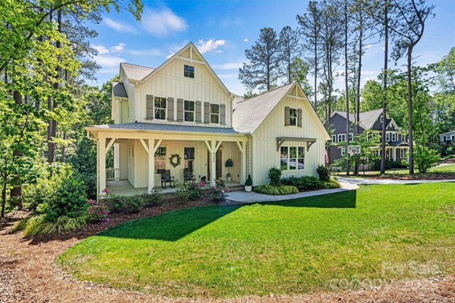 modern farmhouse style home with a shingled roof, board and batten siding, covered porch, and a front yard