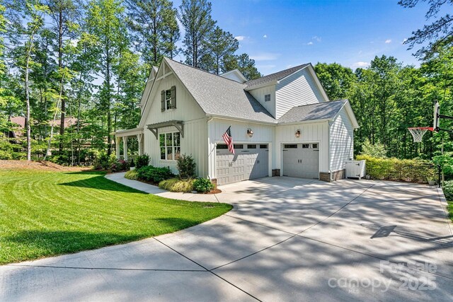 view of side of property with board and batten siding, driveway, roof with shingles, a garage, and a yard