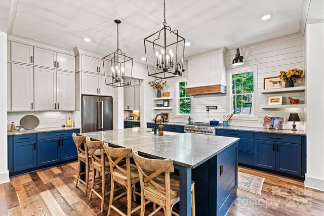 kitchen featuring open shelves, light wood finished floors, blue cabinetry, premium range hood, and high quality fridge