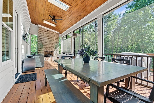 sunroom featuring a skylight, a brick fireplace, outdoor dining space, and a wealth of natural light