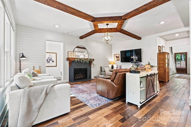living room with dark wood-style flooring, beam ceiling, wooden walls, a fireplace with flush hearth, and a notable chandelier