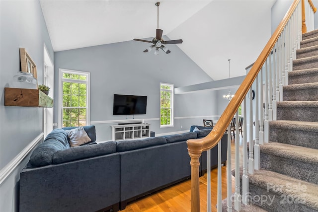 living room featuring ceiling fan with notable chandelier, wood finished floors, stairway, and high vaulted ceiling