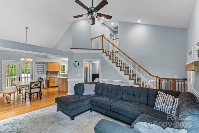 living room featuring high vaulted ceiling, light wood-style flooring, ceiling fan with notable chandelier, visible vents, and stairway