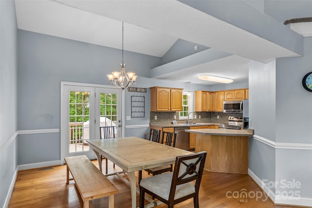 dining space with baseboards, a chandelier, light wood-style flooring, and vaulted ceiling
