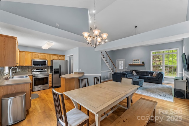 dining space with stairs, a notable chandelier, light wood-style flooring, and lofted ceiling