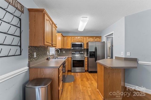 kitchen featuring appliances with stainless steel finishes, tasteful backsplash, a sink, light wood finished floors, and a peninsula