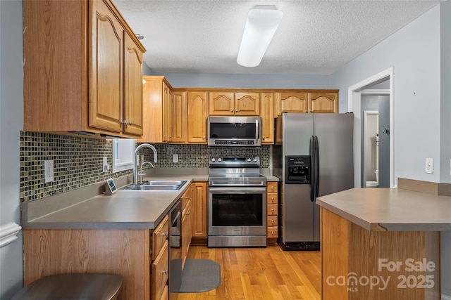 kitchen featuring light wood-style floors, a textured ceiling, a sink, backsplash, and stainless steel appliances
