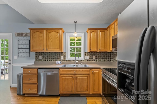 kitchen with a sink, appliances with stainless steel finishes, tasteful backsplash, and light wood-style flooring
