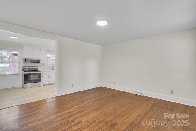 unfurnished living room featuring a sink, visible vents, light wood finished floors, and baseboards