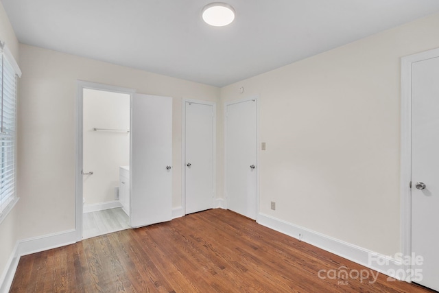 unfurnished bedroom featuring connected bathroom, wood finished floors, and baseboards