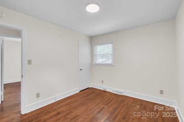 unfurnished room with dark wood-style floors, visible vents, and baseboards