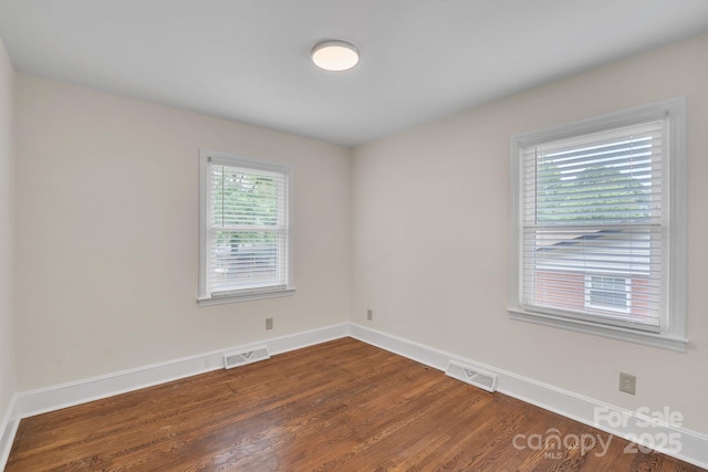 spare room featuring dark wood-style floors, visible vents, and baseboards