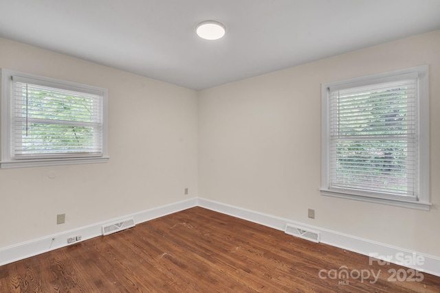 unfurnished room with visible vents, dark wood-style floors, and baseboards