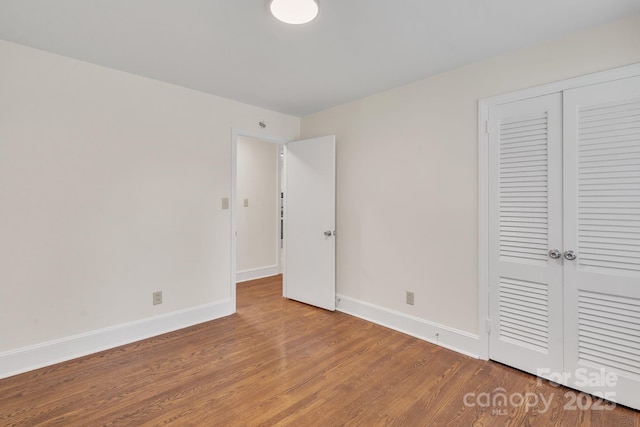 unfurnished bedroom featuring baseboards, wood finished floors, and a closet