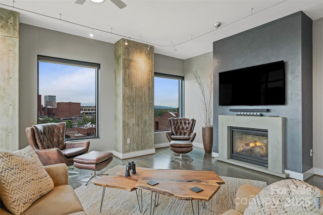 living area with baseboards, a glass covered fireplace, ceiling fan, and wood finished floors