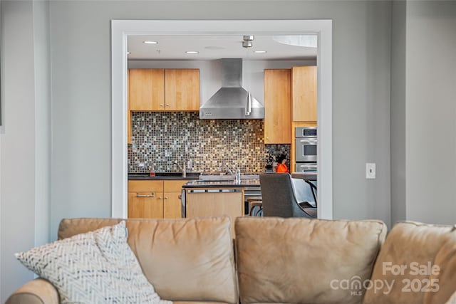 kitchen featuring wall chimney range hood, dark countertops, a sink, tasteful backsplash, and modern cabinets
