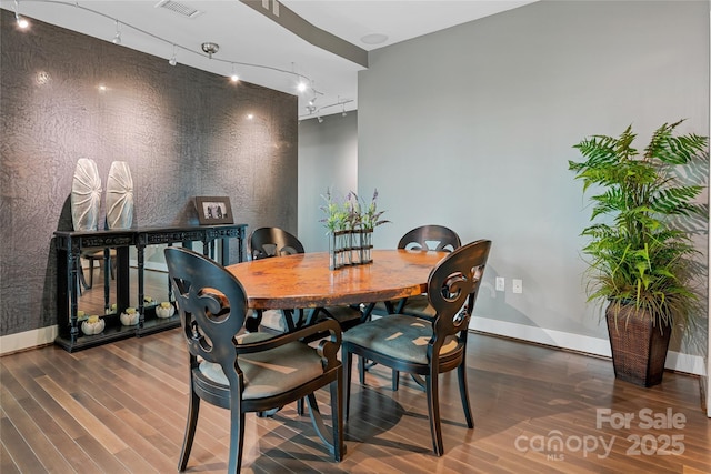 dining room featuring baseboards, rail lighting, visible vents, and wood finished floors