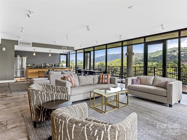 living room with visible vents, floor to ceiling windows, baseboards, and wood finished floors