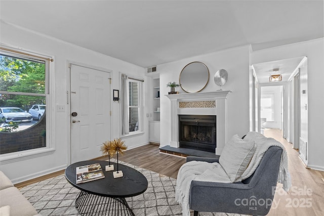 living room with visible vents, built in features, light wood-type flooring, baseboards, and a fireplace with raised hearth
