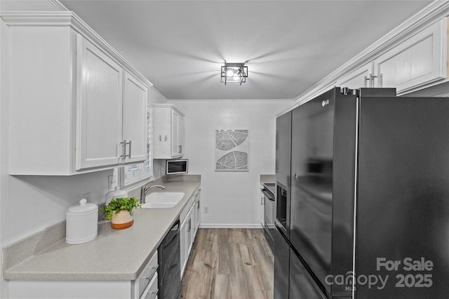 kitchen featuring light countertops, white cabinets, a sink, light wood-style flooring, and black appliances
