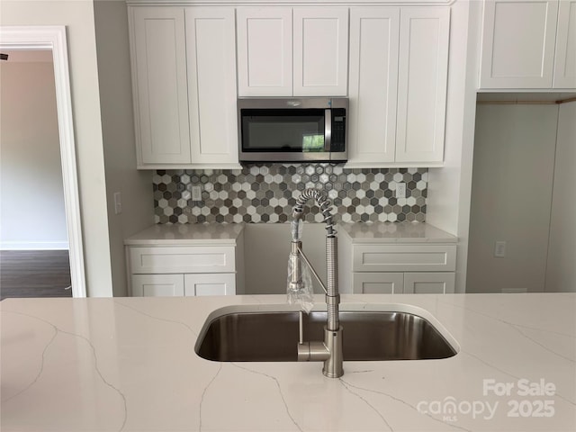 kitchen featuring light stone counters, stainless steel microwave, backsplash, and a sink