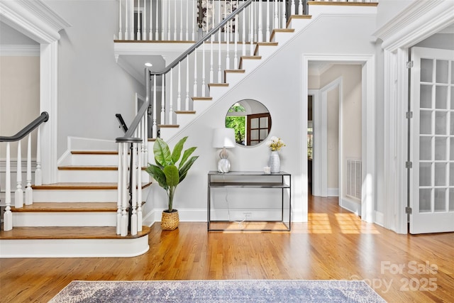entrance foyer featuring baseboards, wood finished floors, visible vents, ornamental molding, and stairway