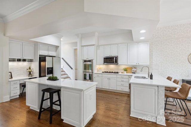 kitchen with a sink, appliances with stainless steel finishes, ornamental molding, and a breakfast bar area