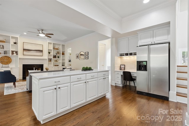 kitchen featuring a ceiling fan, crown molding, a fireplace, white cabinets, and stainless steel fridge