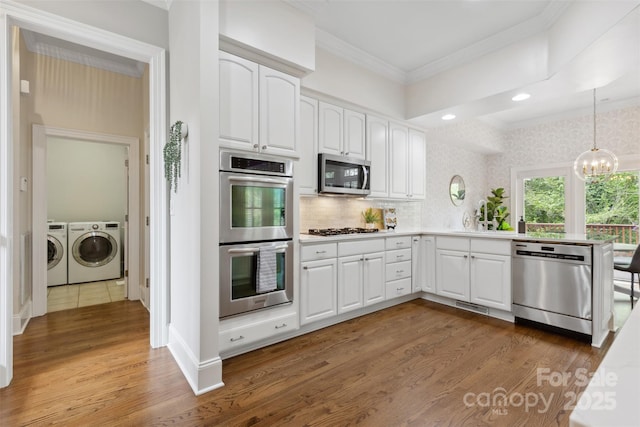 kitchen featuring ornamental molding, washing machine and clothes dryer, wood finished floors, and stainless steel appliances