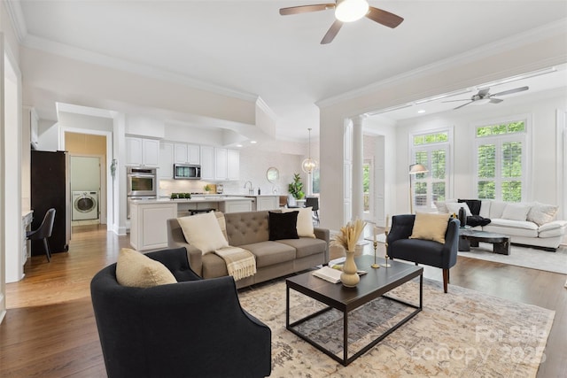 living room featuring crown molding, a ceiling fan, washer / dryer, and wood finished floors