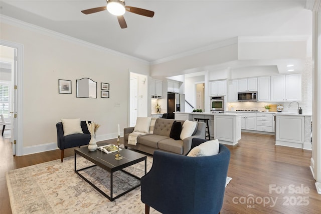 living room with a ceiling fan, baseboards, ornamental molding, and light wood-style floors