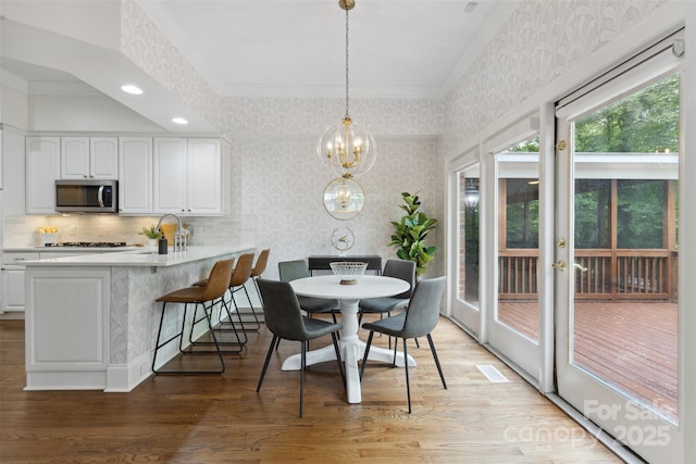 dining space featuring crown molding, light wood-style flooring, an inviting chandelier, and wallpapered walls