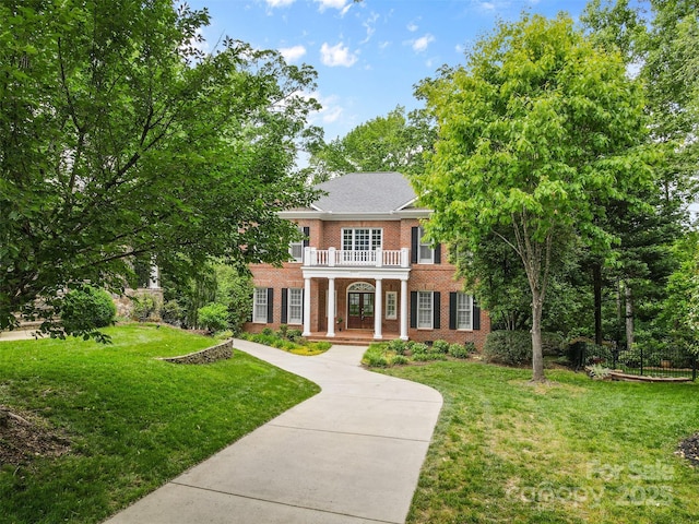colonial house with brick siding, a balcony, a front yard, and covered porch