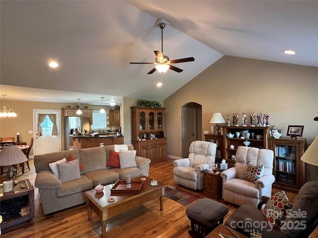 living room featuring wood finished floors, arched walkways, ceiling fan with notable chandelier, and lofted ceiling