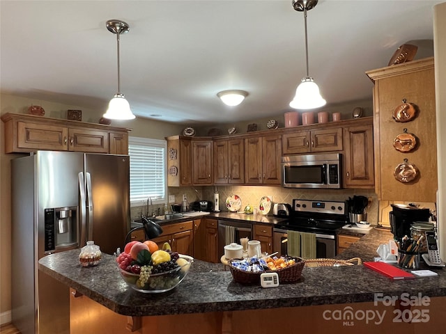 kitchen with appliances with stainless steel finishes, hanging light fixtures, a sink, a peninsula, and backsplash