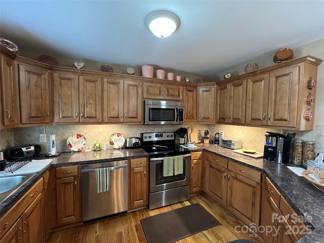 kitchen with dark countertops, stainless steel appliances, brown cabinets, and light wood-style flooring