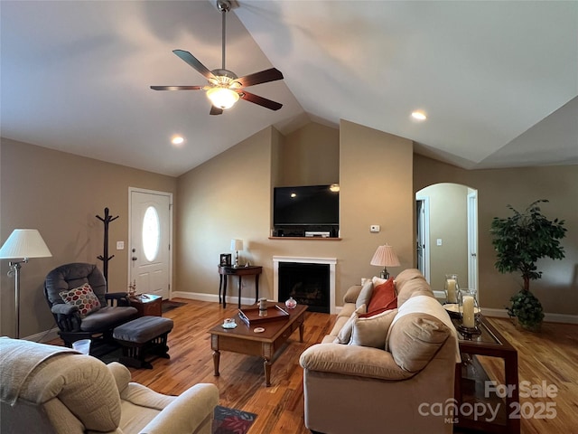 living area featuring baseboards, ceiling fan, arched walkways, light wood finished floors, and vaulted ceiling