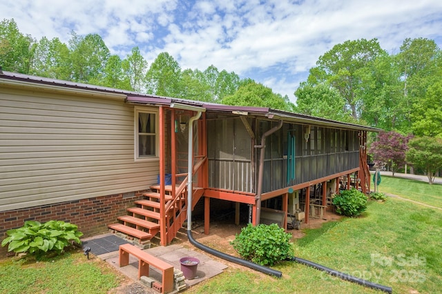 rear view of property with metal roof, a sunroom, a lawn, and stairway