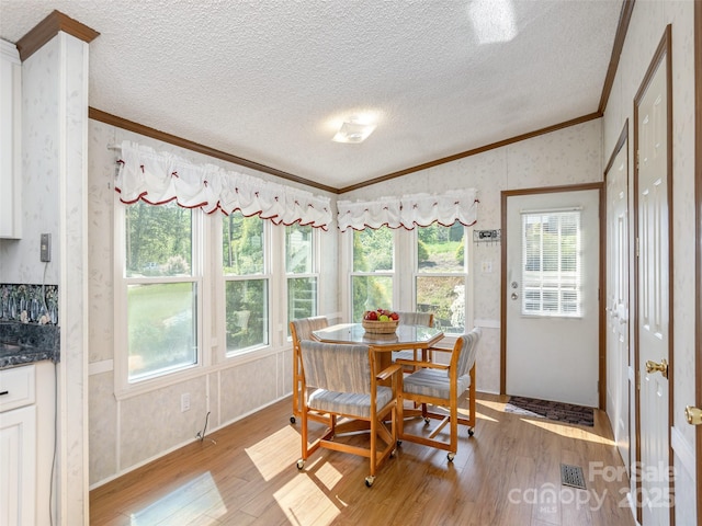 dining area with lofted ceiling, a textured ceiling, crown molding, light wood-style floors, and wallpapered walls