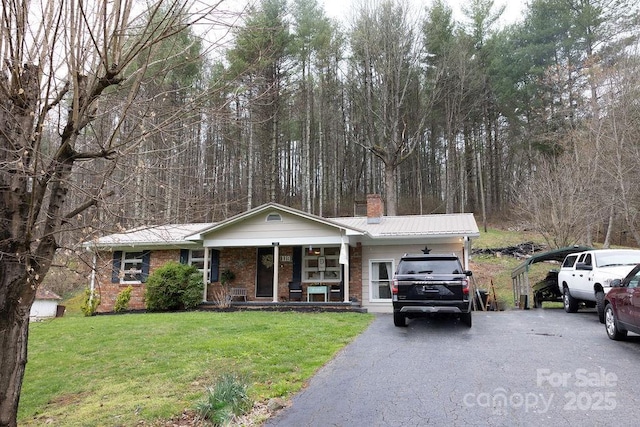 ranch-style home with a front lawn, aphalt driveway, a porch, a chimney, and metal roof