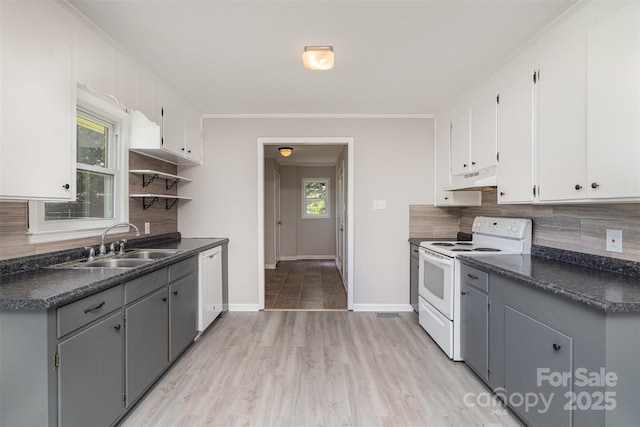 kitchen with under cabinet range hood, white appliances, a sink, backsplash, and dark countertops