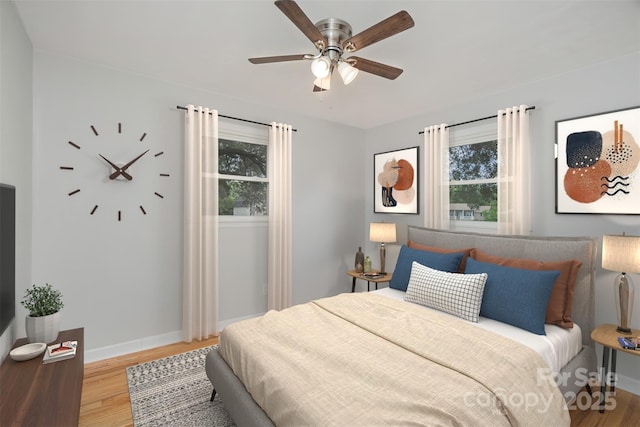 bedroom with wood finished floors, baseboards, and multiple windows
