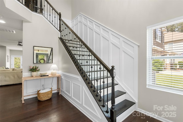 staircase with visible vents, wainscoting, a decorative wall, wood finished floors, and a high ceiling