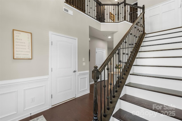 stairs featuring visible vents, a towering ceiling, a wainscoted wall, and wood finished floors