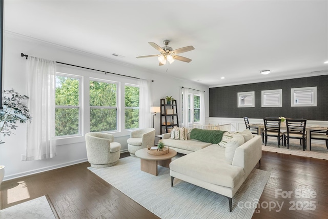 living room featuring crown molding, visible vents, ceiling fan, dark wood-type flooring, and a wainscoted wall